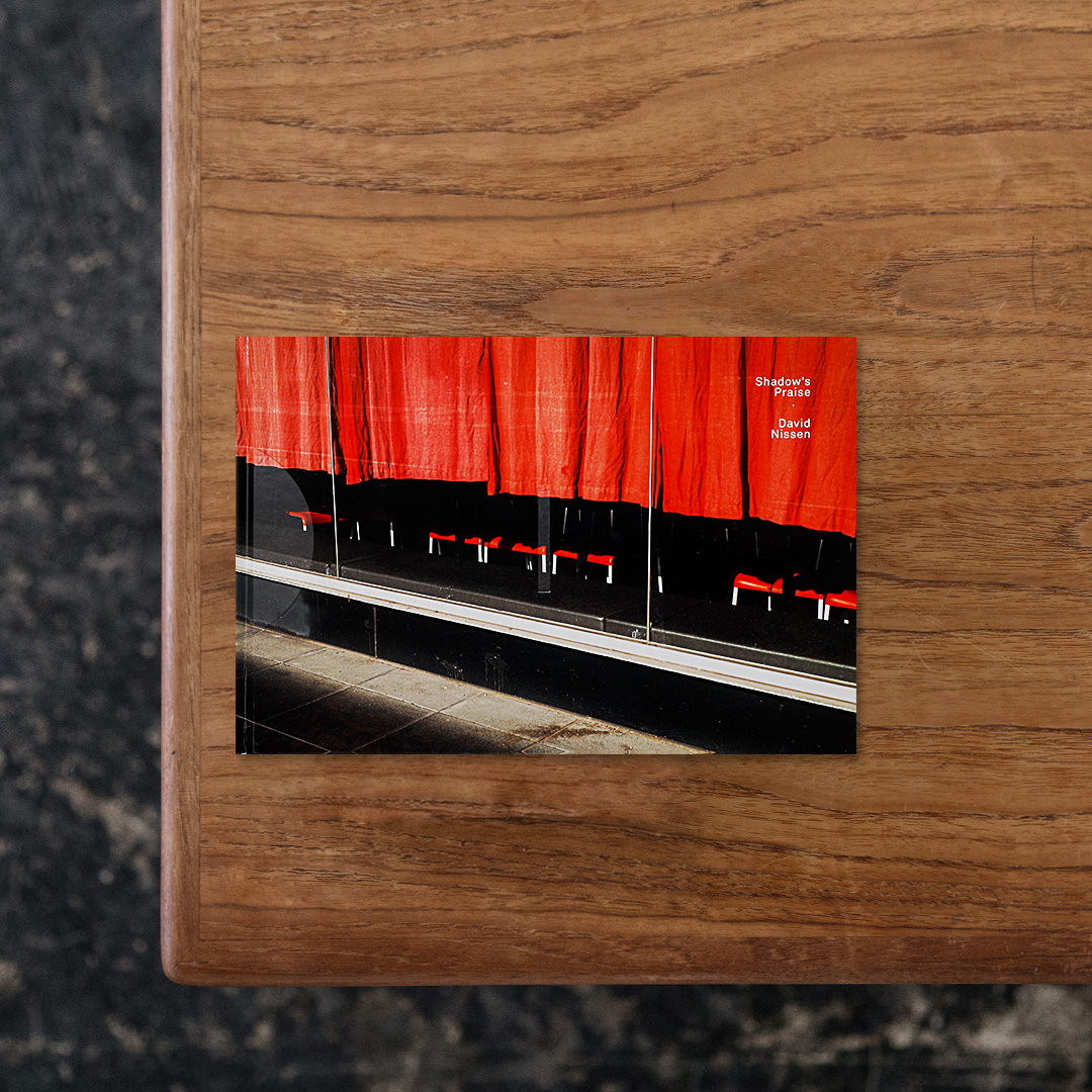 フランス系ベルギー人写真家のDavid Nissen（デイヴィッド・ニッセン）による写真集と、東京在住のサウンドアーティストで映画音楽作曲家のAKHIRA SANOによる音楽をセットに収録した一冊。
フランスの出版レーベル「IKKI」による主導のもと2022年12月から2023年3月にかけて制作された本作では、それぞれが独立した作品として成立しながらも、デュエットとして同時に楽しむことで更なる魅力が引き出されるようになっており、普段は映画の撮影を担当しているデイヴィッドならではの着眼点が光る霧や雨、そして薄れゆく光といった瞑想的なイメージは、SANOによる音楽と共鳴することで、鑑賞者をより一層惹き込みます。

#Shadow'sPraise#DavidNissen#graphic#photo #photograph #designbook #artbook #photobook #photographer#design#art