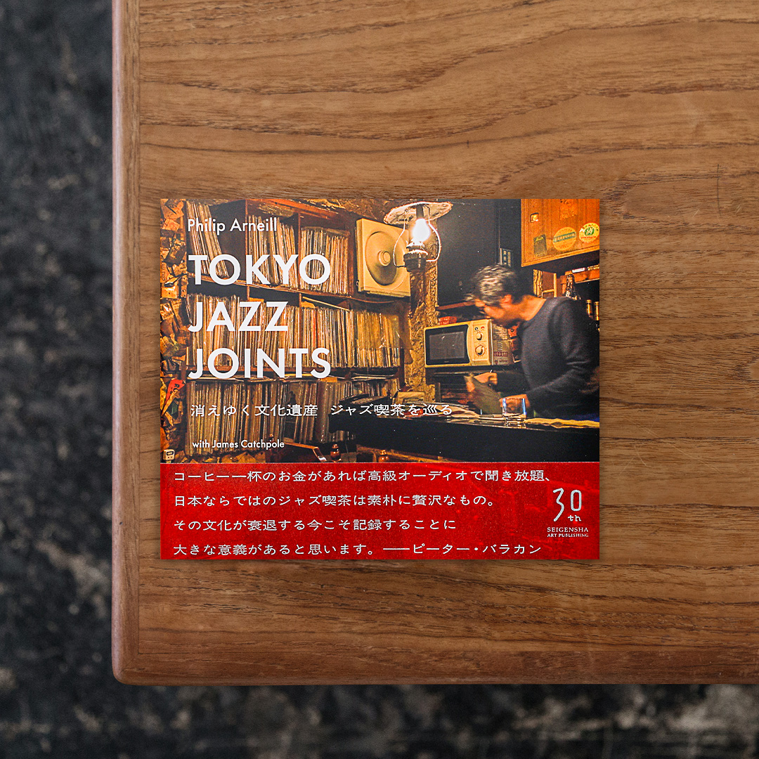 北アイルランド出身の写真家・Philip Arneill（フィリップ・アーニール）が、日本で長期滞在しているアメリカの放送作家・James Catchpole（ジェームス・キャッチポール）からの協力で取り組んだ、日本のジャズバーや喫茶店の様子を記録するプロジェクト「Tokyo Jazz Joints」をまとめた写真集。
日本ではジャズに特化したバーや喫茶店が数多く存在していますが、そうした例は世界においても類がなく、日本独自の文化であるといえます。
しかし音楽趣向の変化や顧客の高齢化、または町の再開発の波にゆっくりと飲み込まれ、これまでに培われてきたこの独自の文化も継承されぬまま、知らず知らずのうちにその姿を消しつつあります。
そうした事態を受けて2015年に始まったプロジェクト「Tokyo Jazz Joints」は、形あるうちにジャズバーや喫茶店の光景を写真の中に封じ込めてタイムカプセルのように保存しようとはじまったもの。当初の予定では東京だけでしたが、徐々に神奈川や岩手、京都とその範囲を日本全国へと広がっていきました。
本書では3年半にわたって撮影した写真を店舗名と住所情報とともに収録。
棚いっぱいに埋まったレコード盤と少し掠れた柔らかな音色を奏でるスピーカー、そしてタバコの煙が染み付いた黄ばんだ壁紙の内装には、表層的に真似るだけでは辿り着けない積年の奥深さが宿っています。

#TokyoJazzJoints消えゆく文化遺産ジャズ喫茶を巡る#PhilipArneill#graphic#photo #photograph #designbook #artbook #photobook #photographer#design#art