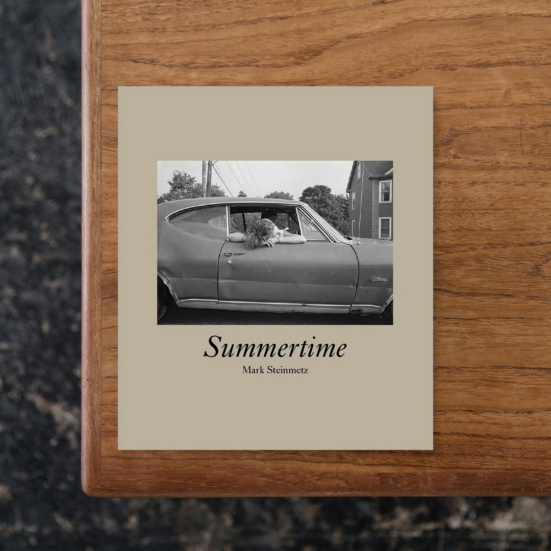 SUMMERTIME

アメリカの写真家・Mark Steinmetz（マーク・シュタインメッツ）が2011年に発表した写真集『Summertime』の増補リマスター版。
今回の新版では、初版の内容に加えてこれまで未発表だった30点の作品を収録し、さらにアメリカのロックバンド Alice Cooper が1972年に発表した楽曲『School's Out』の歌詞も掲載されています。
都市、郊外、田園といったさまざまな場所で夏を過ごす若者や子どもたちを捉えた本作は、1984年から1991年にかけて撮影された。ボストンやシカゴ、コネチカット州ニューヘイブン、イリノイ州の田舎など、当時20代前半だったマークが暮らしていた場所や、両親を訪ねて足を運んだ土地など、彼にとって馴染み深い地域が舞台となっています。
当時のアメリカでは、子どもたちは現在ほど厳しく見守られることなく、また携帯電話やゲーム機といったデジタルデバイスにも縛られず、スケートボードや自転車、木登り、プールや川遊びなど、それぞれの時間を自由に過ごしていました。
そうした子どもたちに向けられたマークの眼差しには、土地への親しみから生まれる穏やかさと安心感が宿っており、気負いのない自然な距離感が写真全体に静かに漂っています。

#SUMMERTIME#MarkSteinmet##graphic#photo #photograph #designbook #artbook #photobook #photographer#design#art